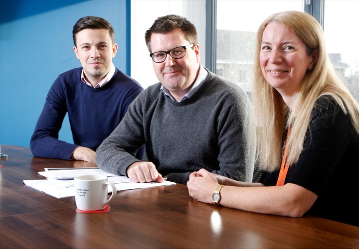 Three Ultimate Finance employees posing and smiling in a meeting room