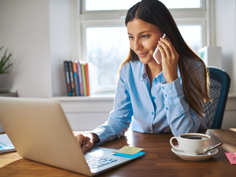 A causally dressed businesswoman making a phone call while looking at her laptop