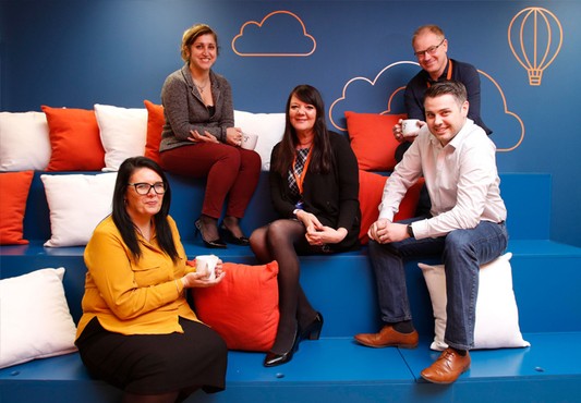 Ultimate Finance employees posing on blue, orange and white stalls in the Bristol office
