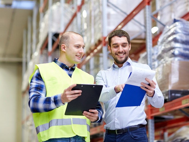 Two smiling employees in a warehouse discussing orders